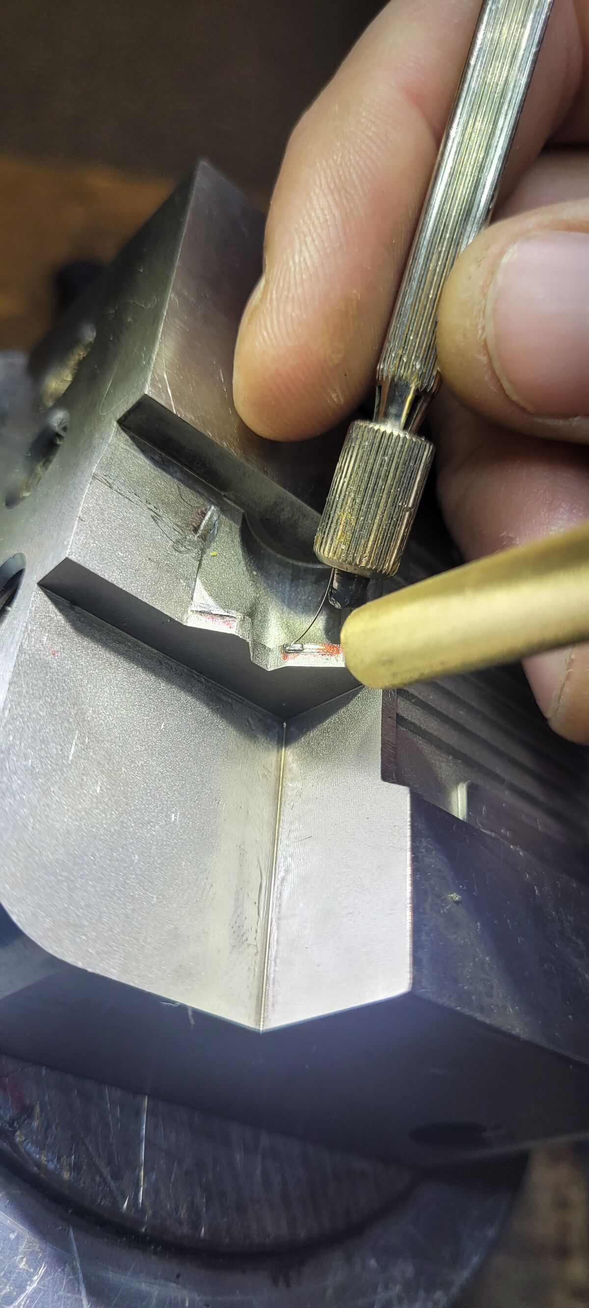 Hand führt Zusatzdraht an ein eingespanntes Werkzeugbauteil, darüber die Düse des Mikrolasers.